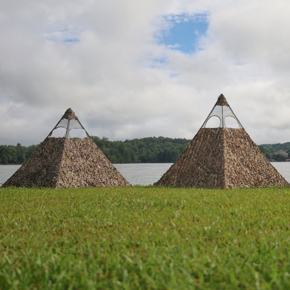 One Nukem Blind and one Nukem XL Blind in mossy oak country roots placed on the grass next to each other in front of a lake to show size comparison
